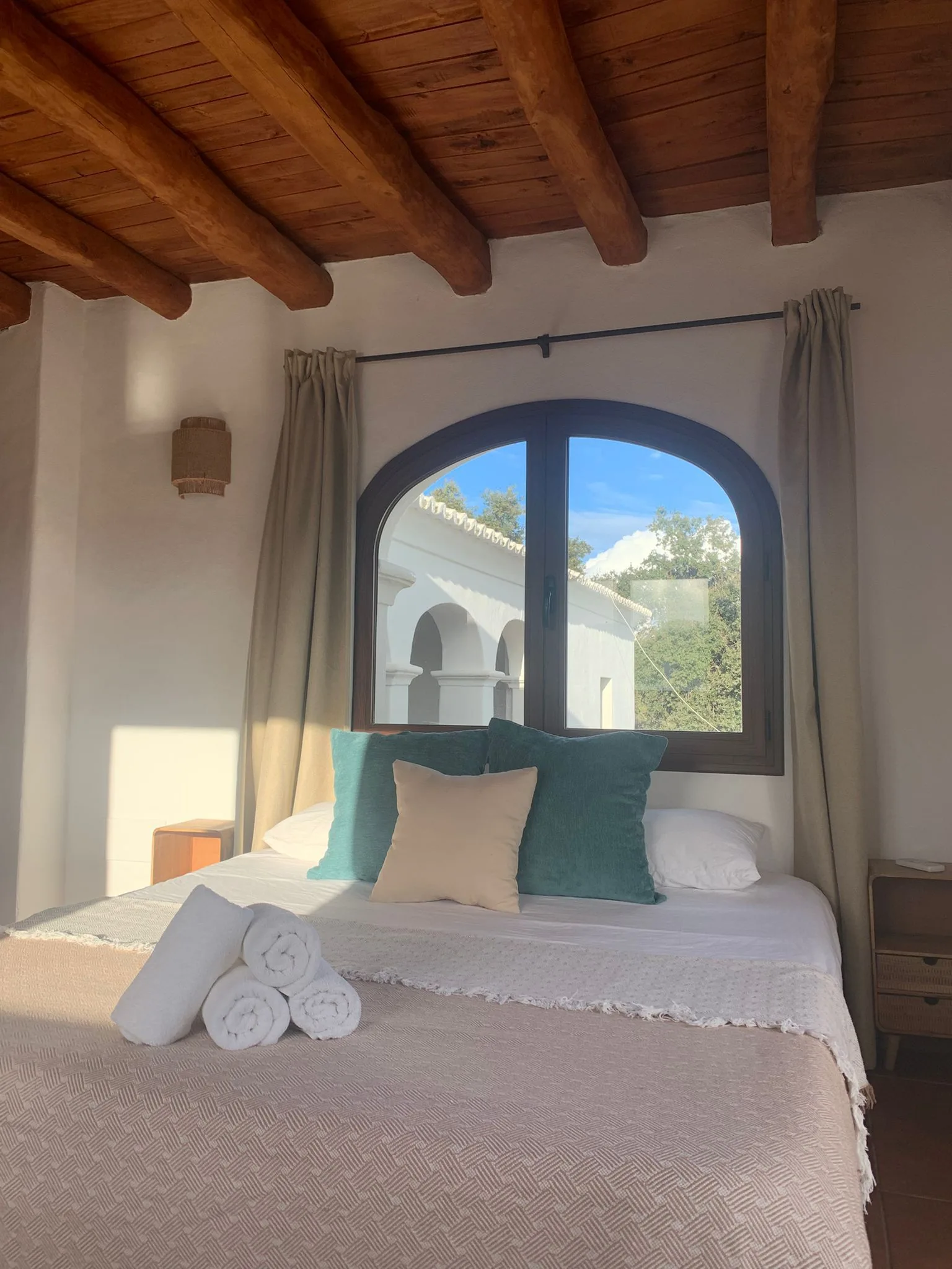 Finca bedroom with arched window, teal cushions and wooden beams — Habitaciones Ibiza